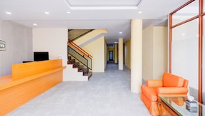 Una zona de recepción con un mostrador de madera, una escalera y un sofá naranja.