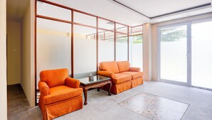 Una habitación con dos sillones naranja, una mesa de centro de vidrio y un ventanal corredero que da a un espacio al aire libre.