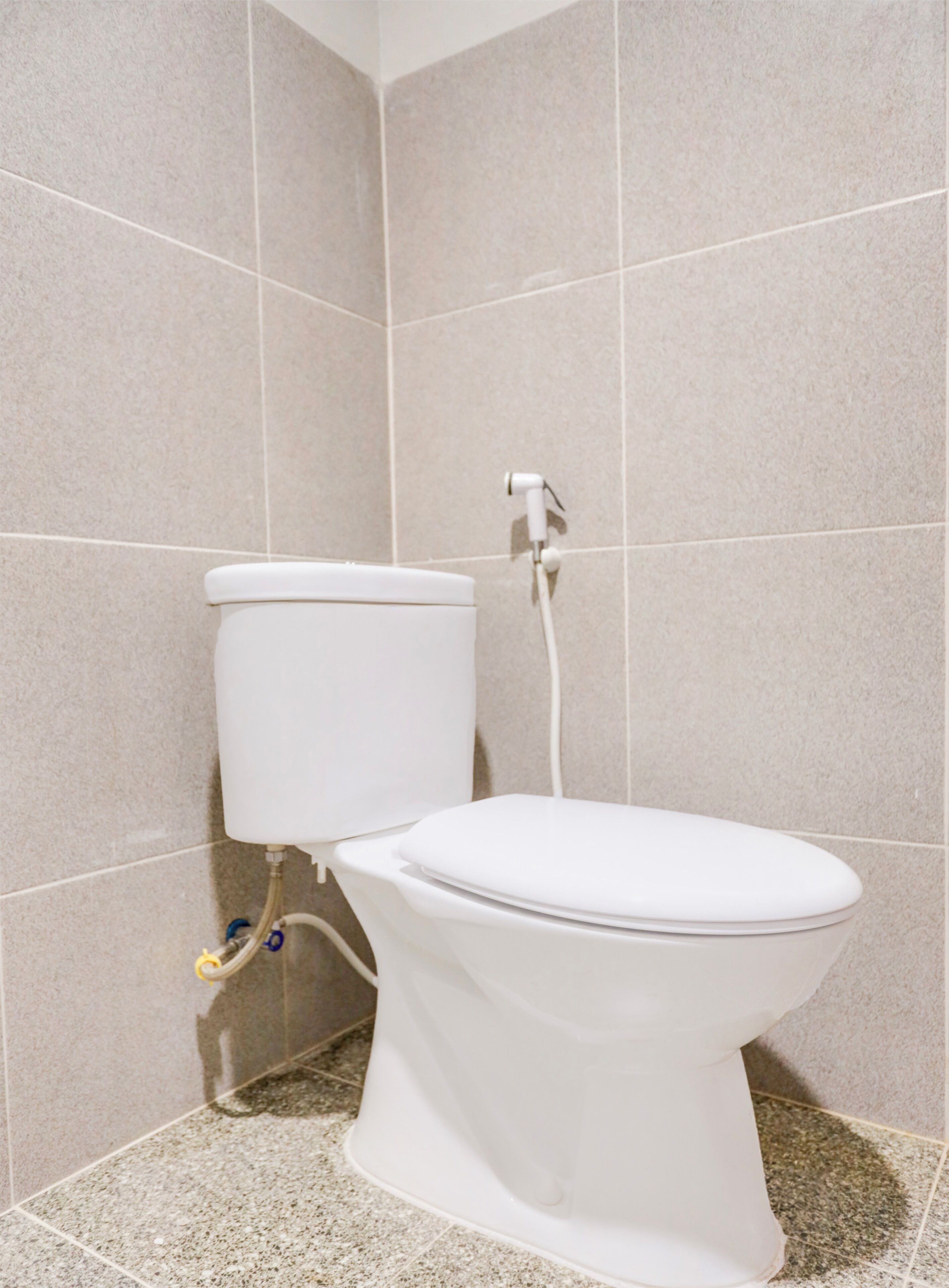 Inodoro blanco con tanque y palanca de descarga, frente a una pared de azulejos con un diseño similar.