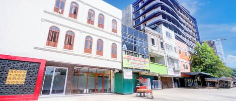 A street view with a white building with red shutters, a modern blue building, and a green storefront.