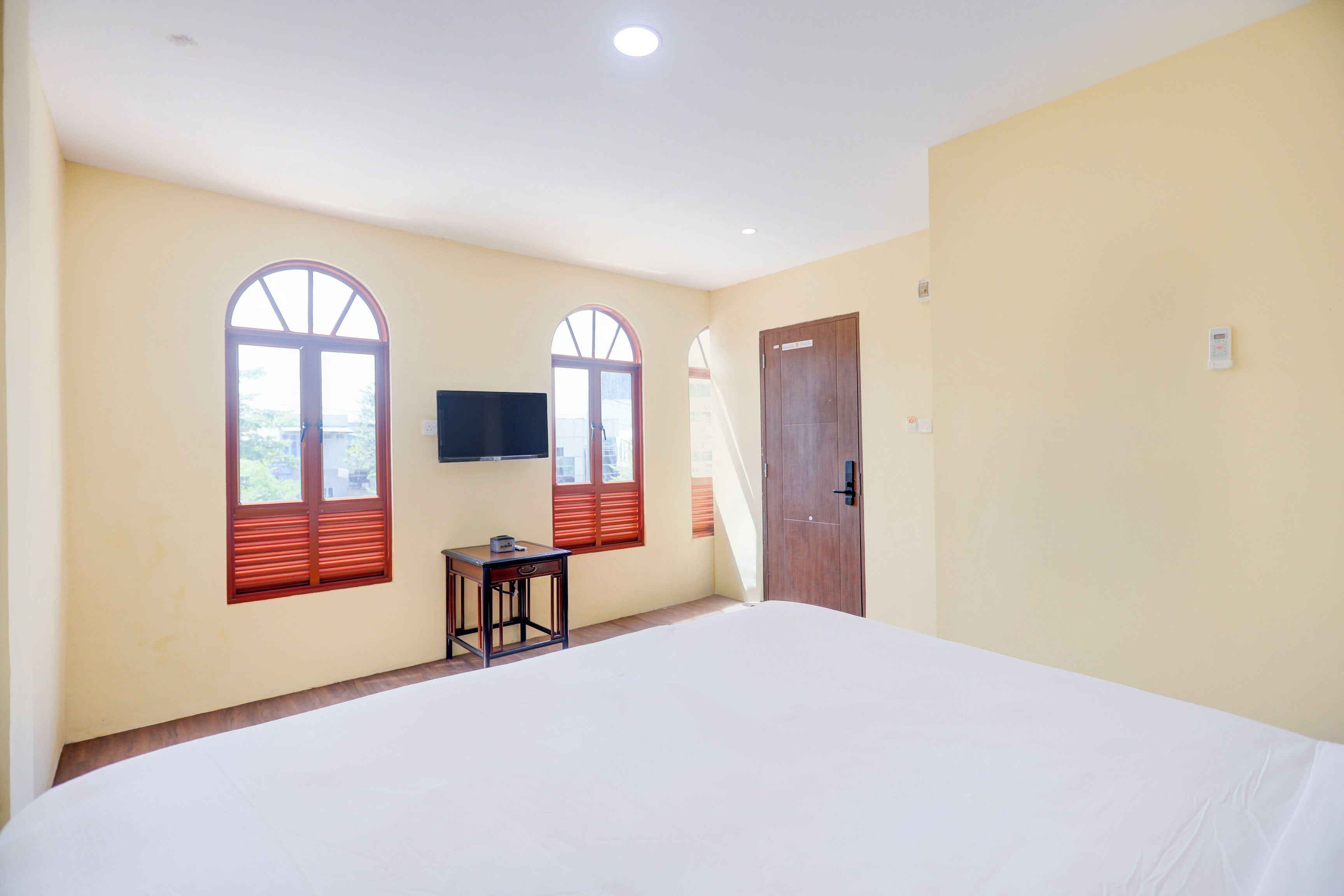 Une chambre avec un grand lit, deux fenêtres avec volets, un téléviseur fixé au mur et une porte.