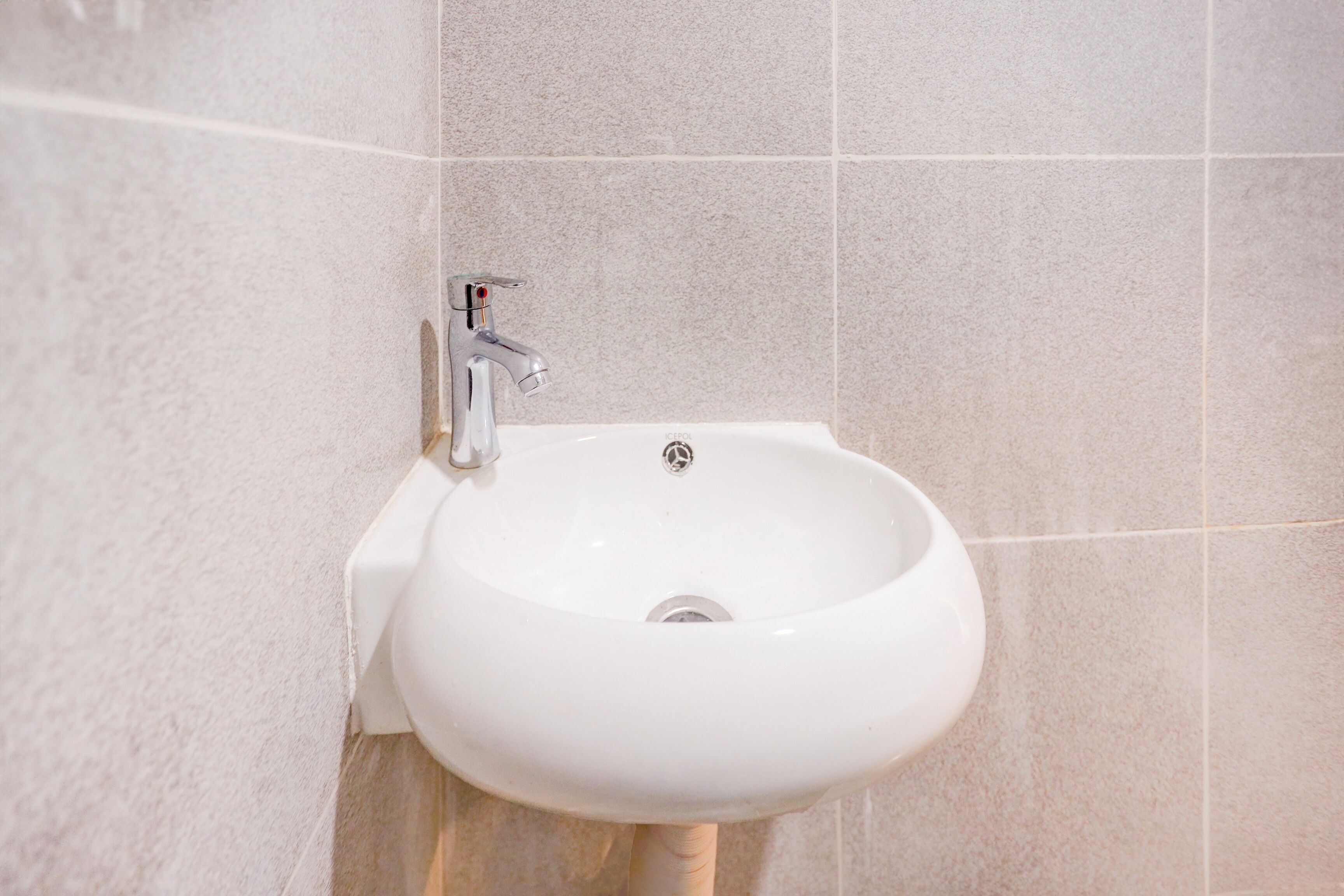 A white bathroom sink with a modern faucet, mounted on a tiled wall.