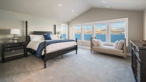 Ein Schlafzimmer mit einem großen Bett, einem Nachttisch, einer Kommode und Meerblick durch große Fenster.