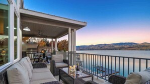 Ein Balkon mit Korbmöbeln, einem Tisch mit Kerzen und Blick auf Wasser und Hügel.
