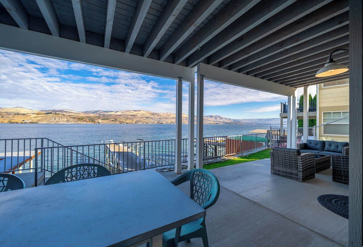 A covered outdoor area with a table and chairs, a sofa, and a view of a body of water and distant hills.