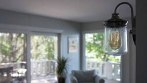 Ett rum med en hängande lampa, en stol, ett litet bord och utsikt genom stora fönster.