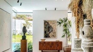 A modern living room with a wooden floor, a large painting, a wooden cabinet, and a stone sculpture.