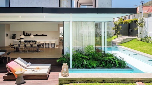 A modern house with a glass-enclosed patio, a pool, and a dining area.