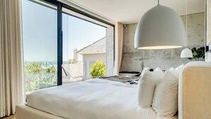 A modern bedroom with a large bed, a view of the outdoors, and a pendant light.