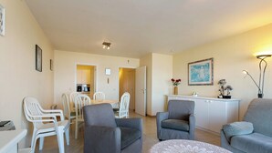 A modern living room with grey sofas, a dining area with white chairs, and a kitchen in the background. - Apartment in Blankenberge Near the Beach (Blankenberge)