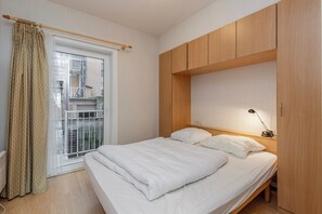 A bedroom with a bed, wooden wardrobe, and a window with a view of a building. - Apartment in Blankenberge Near Seafront (Blankenberge)