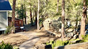 A forested area with a wooden deck, a stone bench, and a paved path. - Rock Haven - Prescott Cabin Rentals (Prescott)