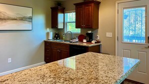 A kitchen with granite countertops, wooden cabinets, a built-in dishwasher, and a window with blinds. - Rock Haven - Prescott Cabin Rentals (Prescott)