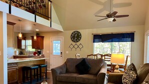 A spacious living area with a high ceiling, a kitchen with dark wooden cabinets, a large wall clock, and a comfortable seating arrangement. - Rock Haven - Prescott Cabin Rentals (Prescott)