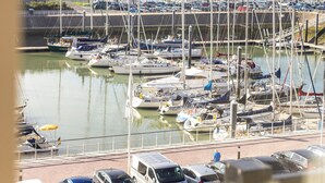 Ein Yachthafen mit zahlreichen Schiffen, ein Parkplatz mit Autos und Gebäude im Hintergrund.