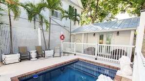 A pool area with a white fence, lounge chairs, and a small building with a porch. - Sailfish Suite on Duval (Key West)