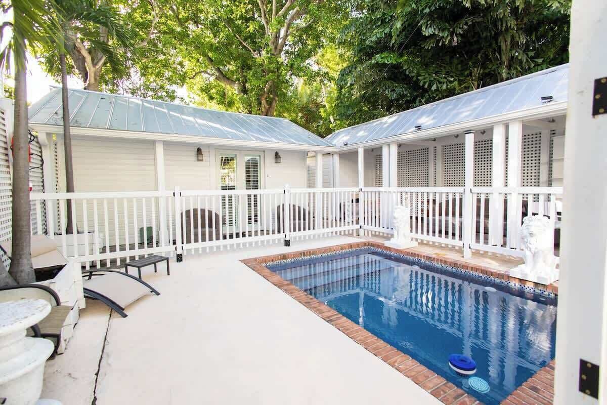 A pool area with a white fence, lounge chairs, and a covered seating area.