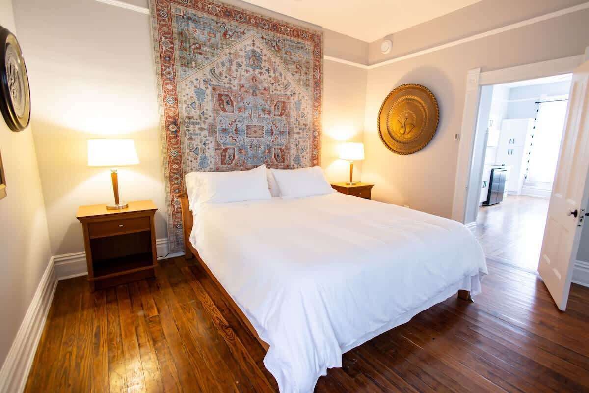 Une chambre à coucher avec un grand lit, un plancher en bois, une tapisserie à motifs, deux lampes de chevet et une horloge murale ronde.
