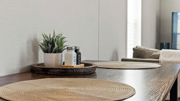 Une table en bois, agrémentée de sets de table en fibres tressées, d’une plante en pot, de salières et de poivrières, et d’un plateau.