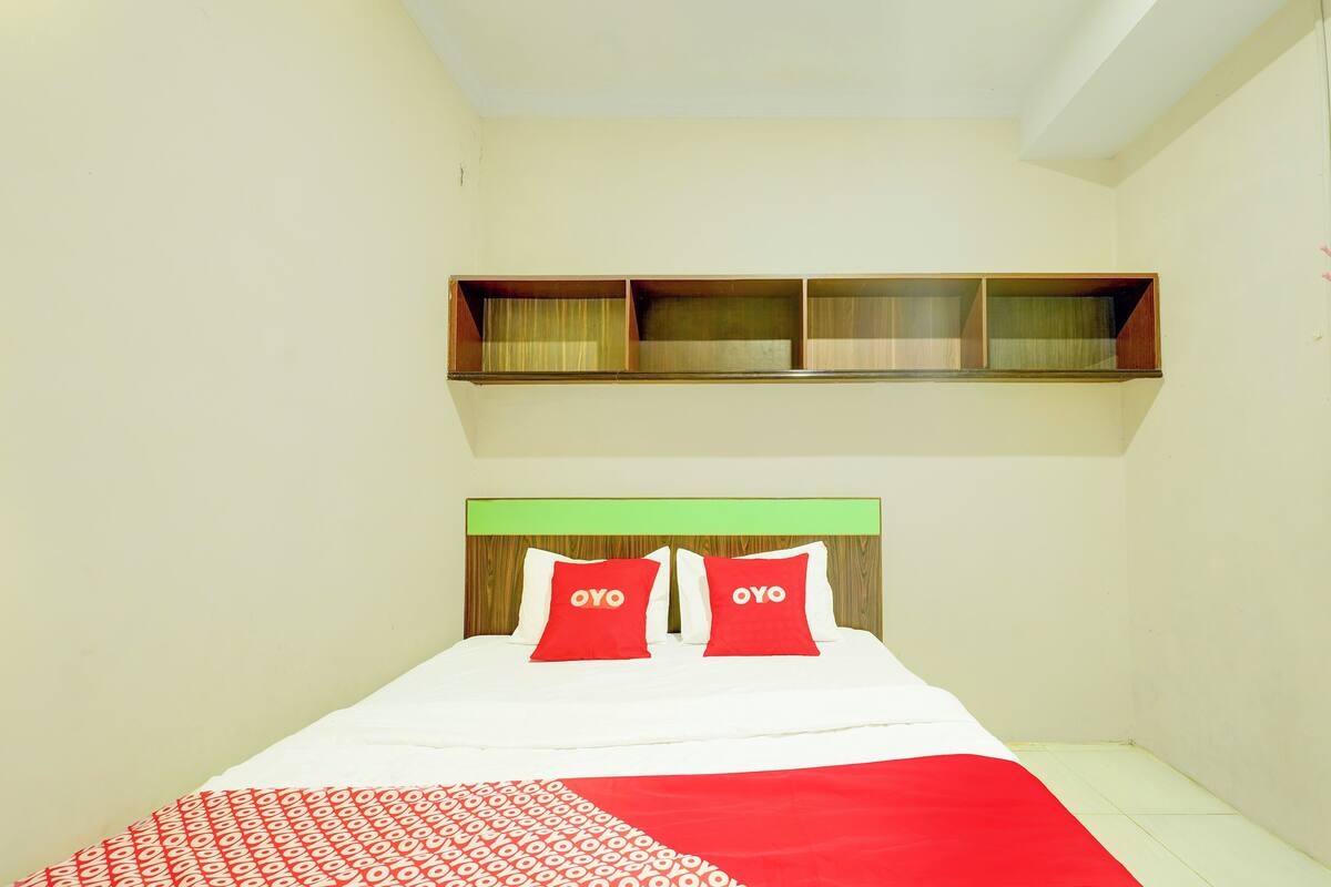 A single bed with a green headboard, two red pillows with "OYO" text, and a red and white patterned bedspread.