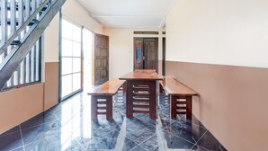 Un pasillo con una escalera, una mesa de madera con bancos y una puerta con un letrero rojo.