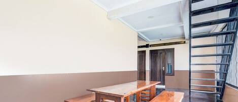 Una habitación con una mesa de madera y bancos, una escalera y una puerta al fondo.