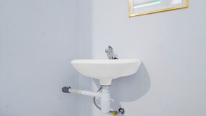 Un lavamanos blanco con grifo cromado, instalado en una pared blanca.