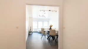 A modern dining area with a round table and chairs, a vase with flowers, and a bright window in the background. - Apartment in Ostend Near Shopping Street (Ostend)