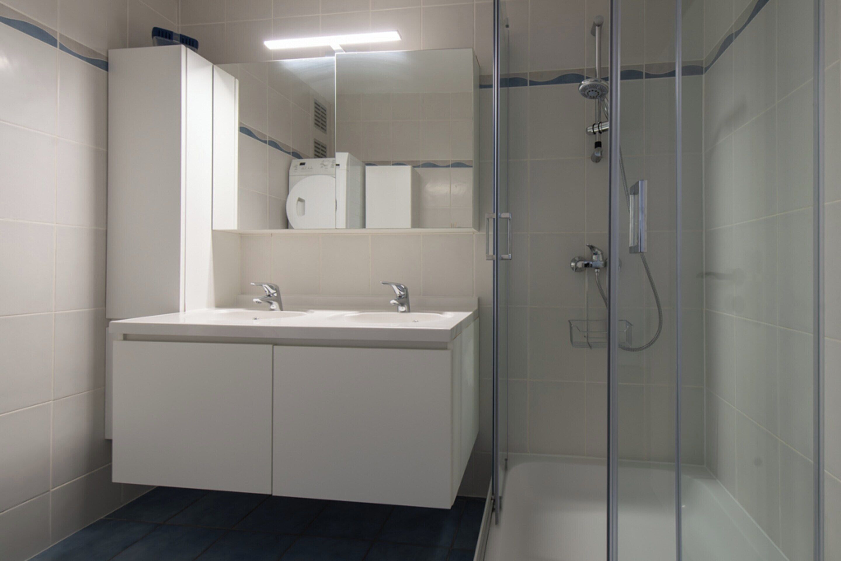 A modern bathroom with a glass-enclosed shower, a double sink vanity, and a mirror above the sink.