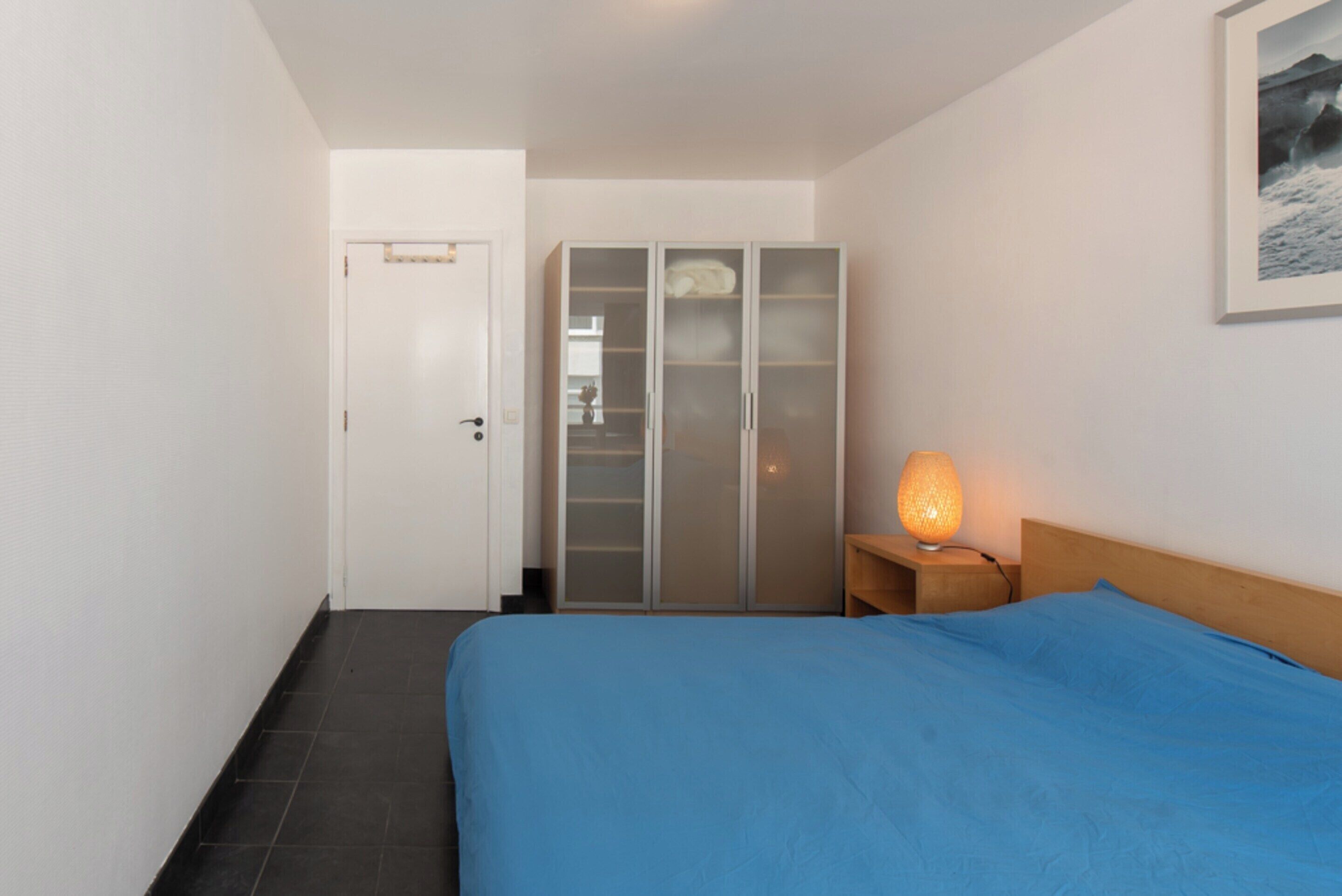 A bedroom with a bed, a wardrobe, a nightstand, and a lamp.
