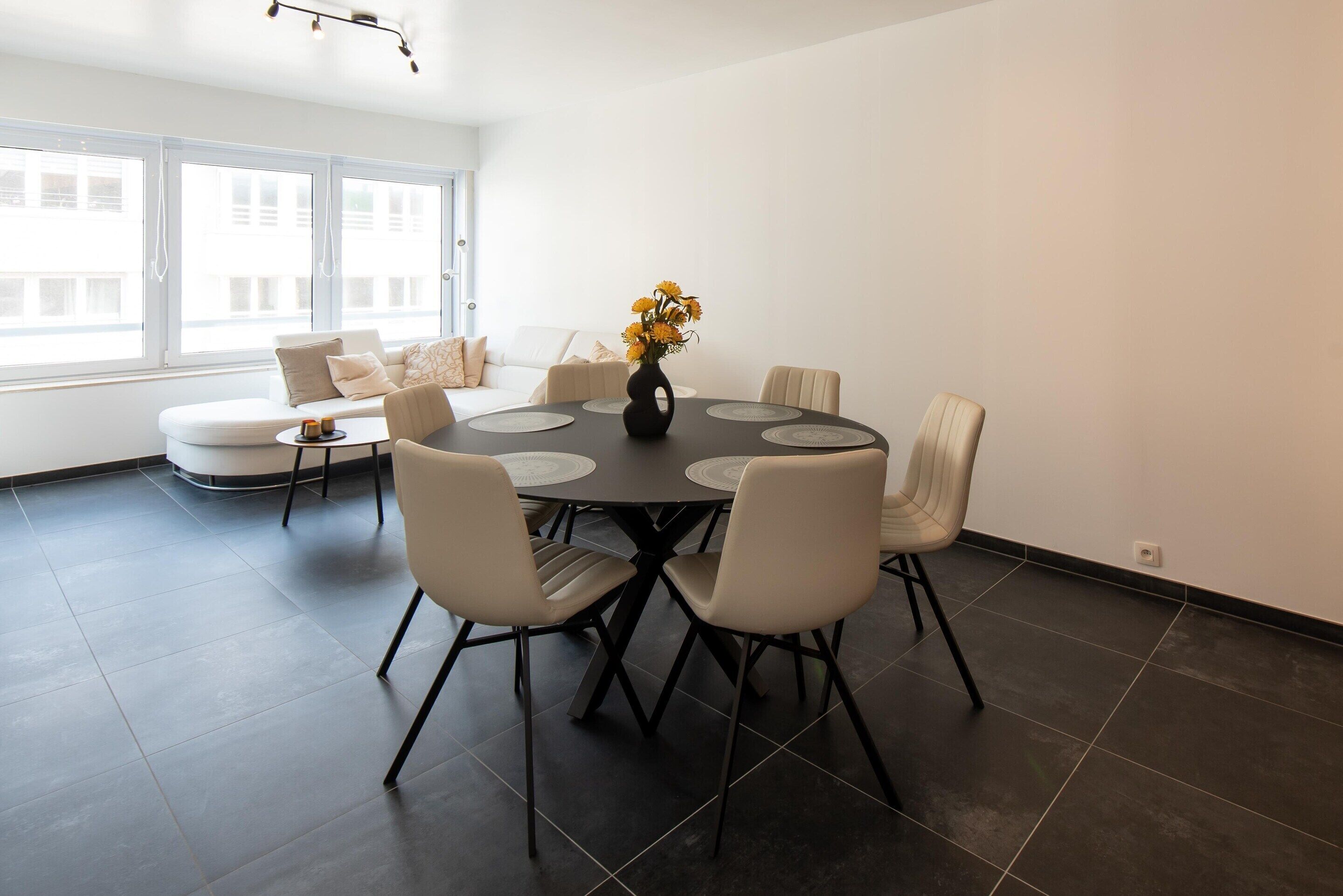 A modern dining area with a round table, six chairs, and a vase of flowers.