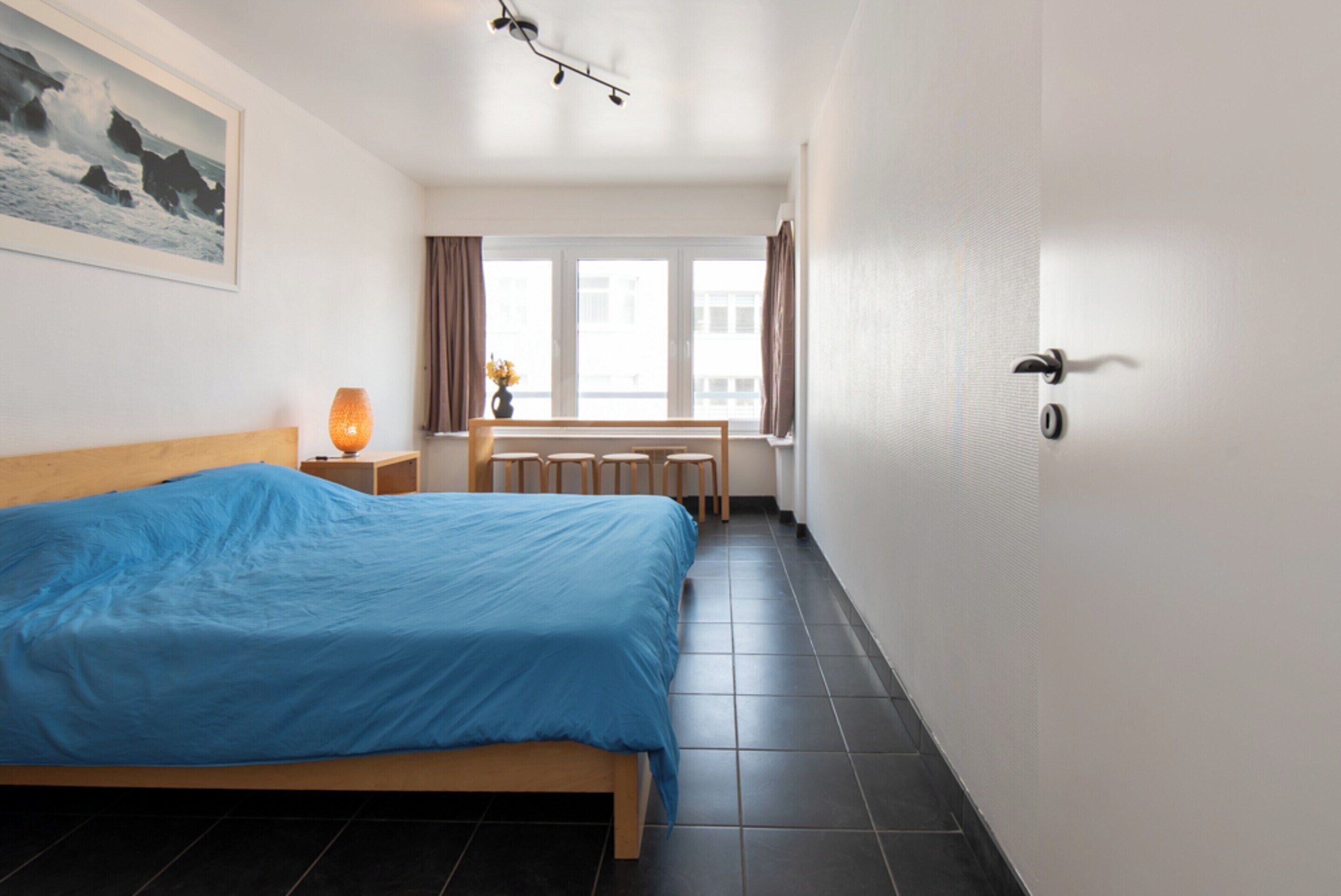 Une chambre d’hôtel avec un lit, une table de chevet, une lampe, une fenêtre avec des rideaux et une vue sur les bâtiments environnants.