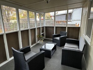 A covered patio with wicker furniture, a potted plant, and a view of the neighborhood.