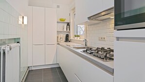A compact kitchen with white cabinetry, a gas stove, a sink, and a window above the counter. - Apartment in Blankenberge Near Seafront (Blankenberge)