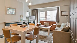 A modern living room with a dining table, sofa, and television. - Apartment in Blankenberge Near Seafront (Blankenberge)