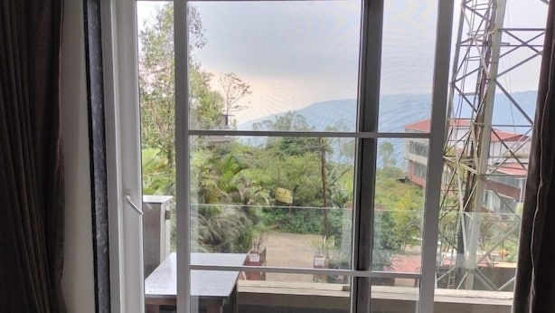 A bedroom with a large sliding glass door leading to a balcony. The room has a bed with a white and gray striped bedspread. - Hotel Om Palace (Mahabaleshwar)
