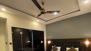 A modern hotel room with a large bed, a ceiling fan, and a glass door leading to a balcony. - Hotel Om Palace (Mahabaleshwar)