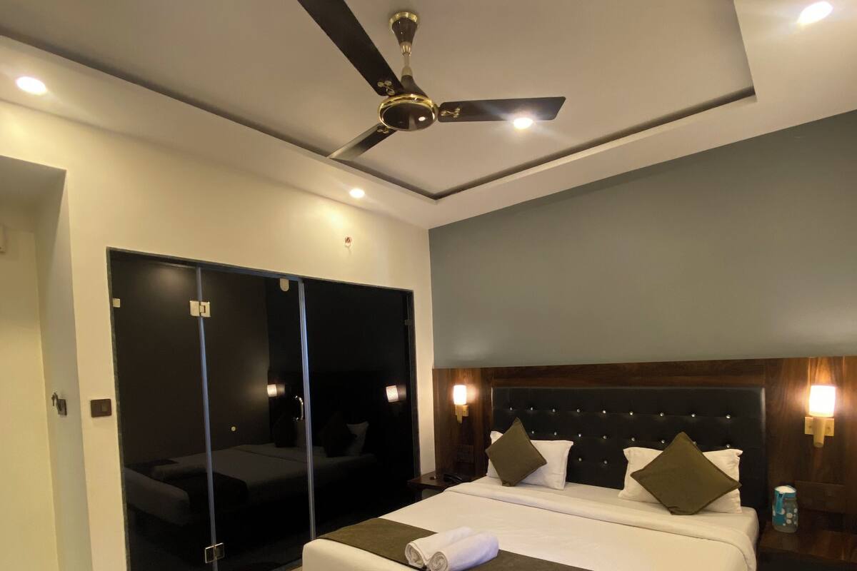 A modern hotel room with a large bed, a ceiling fan, and a glass door leading to a balcony.