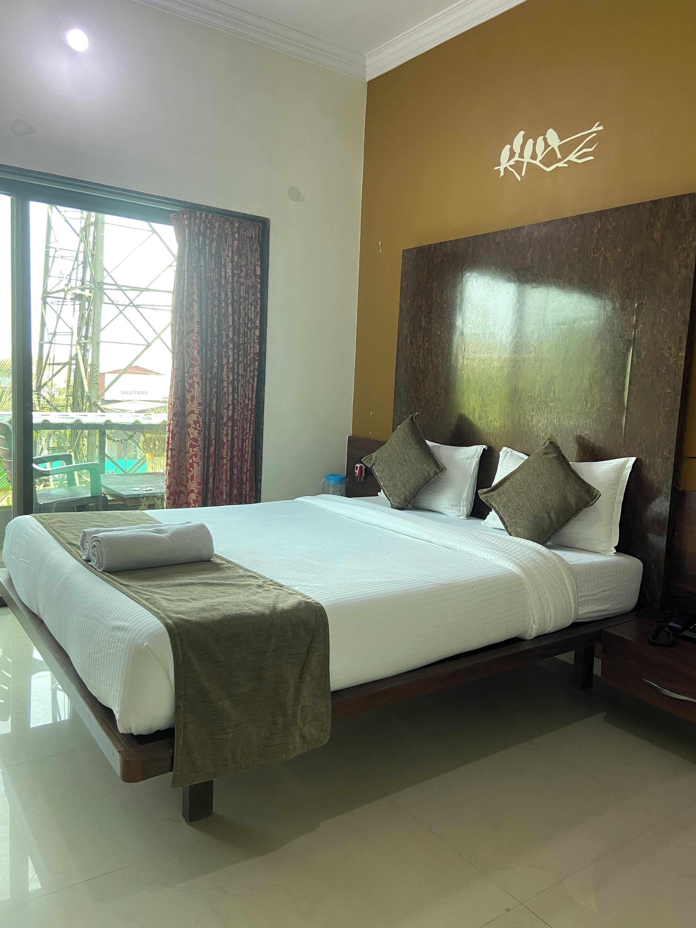 A hotel room with a large bed, a view of a construction site, and a decorative wall with a bird design.