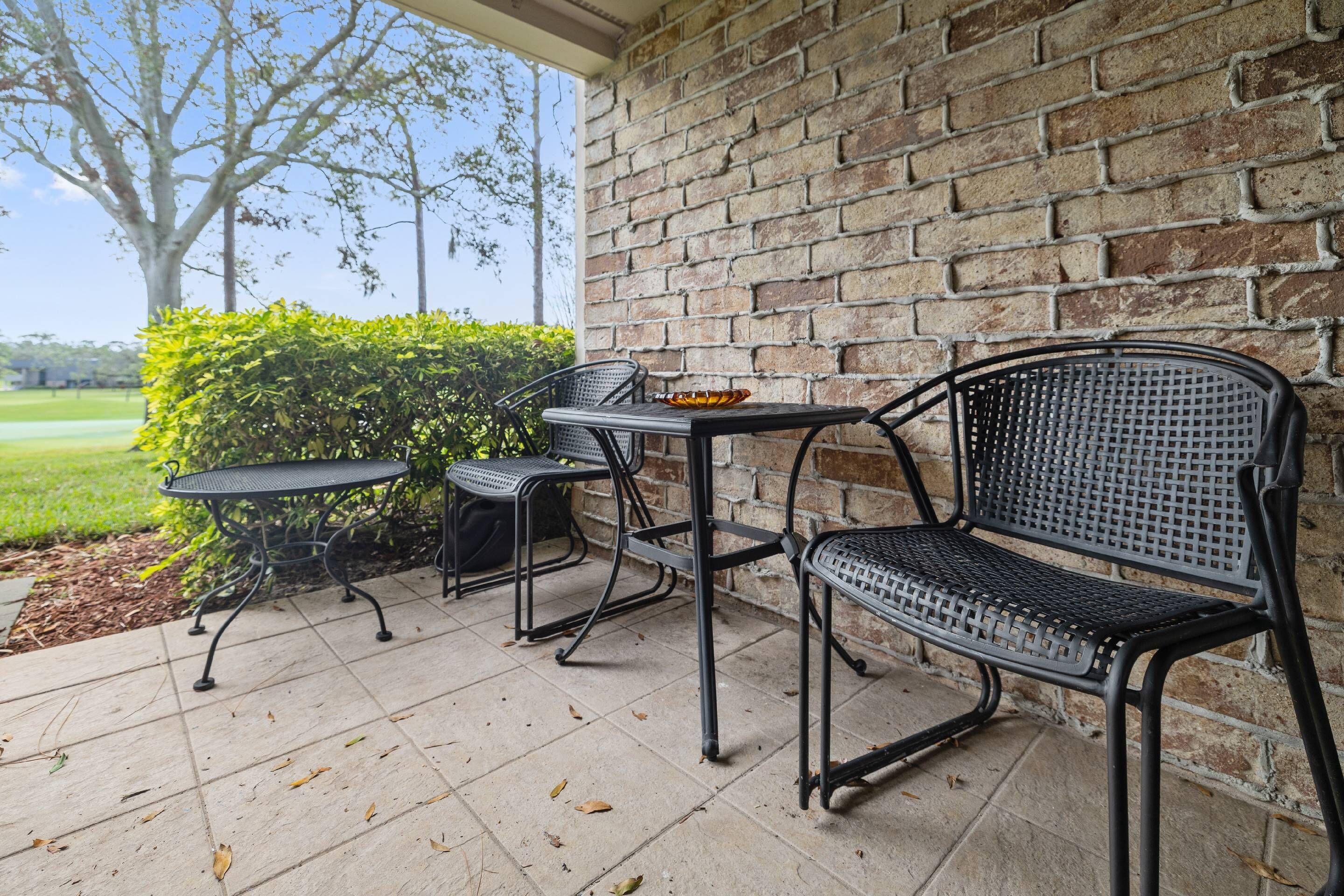 Une terrasse avec un mur en briques, une table en métal et une chaise en métal.