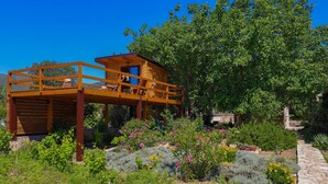 A wooden deck structure with a small cabin, surrounded by lush greenery and flowering plants. - Picturesque Escape Holiday Home With Pool and Sauna (Kastela)
