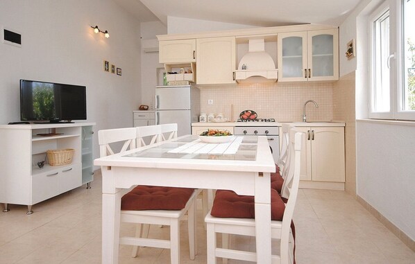 A modern kitchen with white cabinetry, a dining table with red cushions, and a television on a white cabinet. - Picturesque Escape Holiday Home With Pool and Sauna (Kastela)
