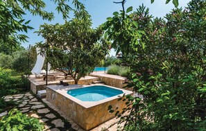 Zona de piscina privada al aire libre con terraza de piedra, sillas de descanso y un pequeño jacuzzi.