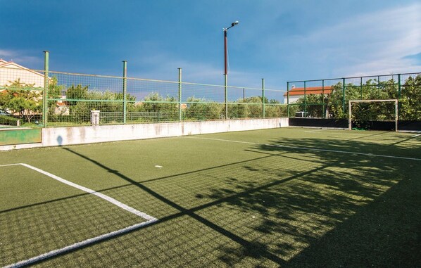 Una cancha de tenis exterior con red, postes de portería y una valla alrededor.