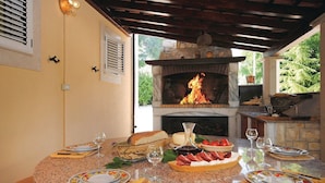 An outdoor kitchen with a stone fireplace and a dining table set for a meal. - Picturesque Escape Holiday Home With Pool and Sauna (Kastela)