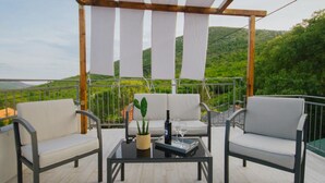 A terrace with two white cushioned chairs, a glass table, and a potted plant.