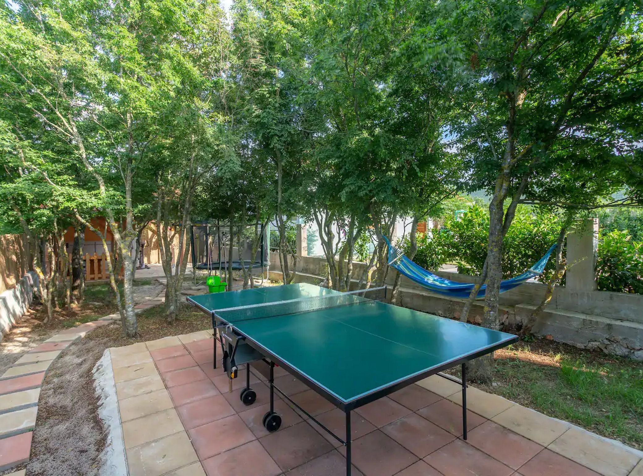 An outdoor table tennis table set up in a garden with trees and a hammock.