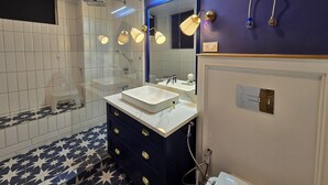 A modern bathroom with a glass-enclosed shower, a vanity with a white sink and dark blue drawers, and a mirror with a blue accent wall. - Hygge Home Manali (Manali)