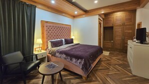 A hotel room with a large bed, a desk, a chair, a ceiling fan, and wooden flooring. - Hygge Home Manali (Manali)