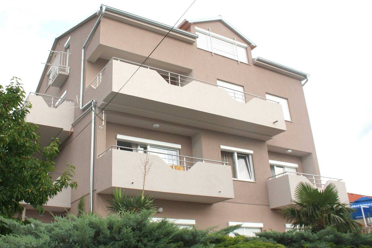 A multi-story residential building with balconies, windows, and a small tree in the foreground.